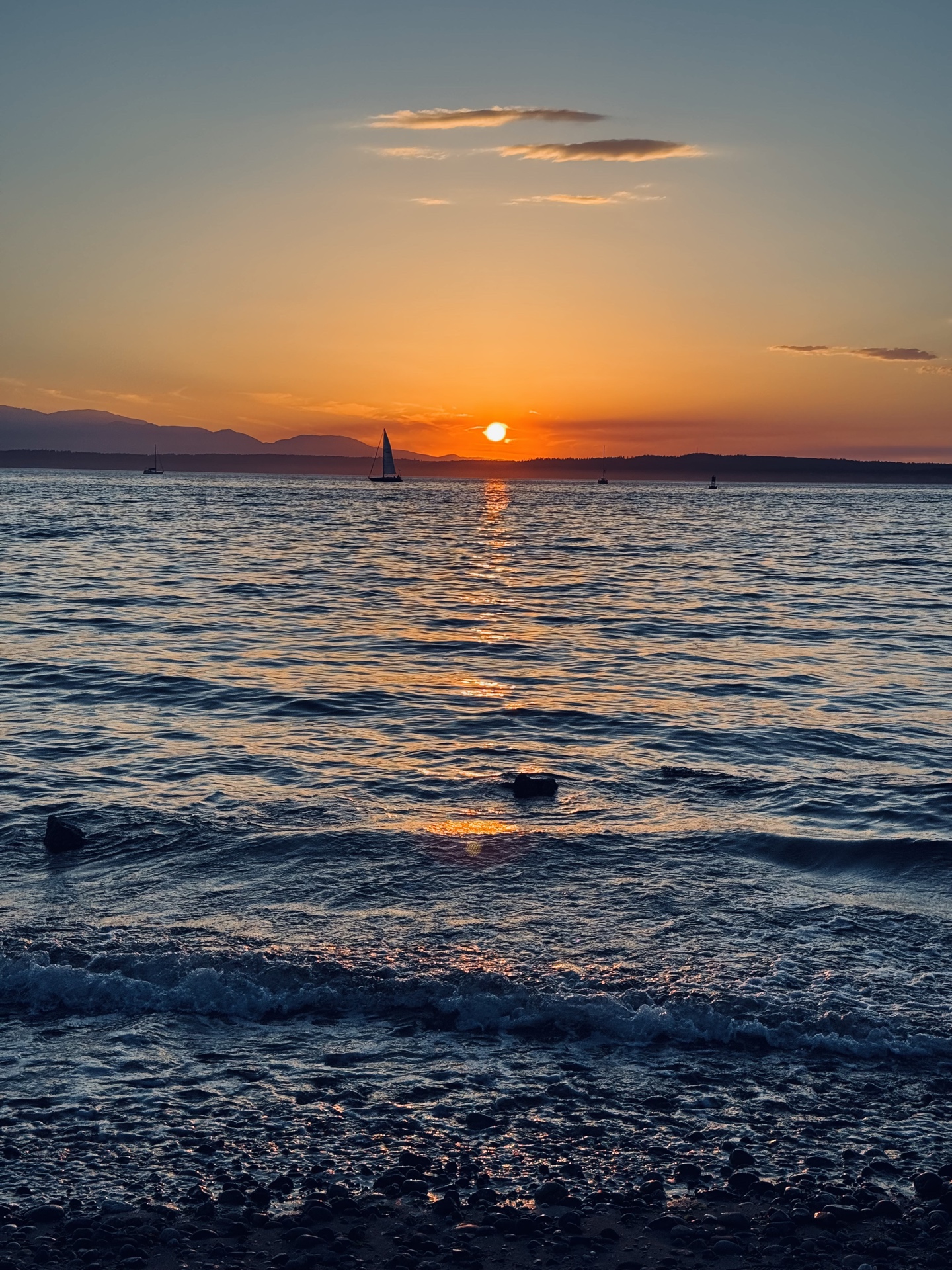 The sun setting over the water, with a sailboat silhouetted near the horizon.