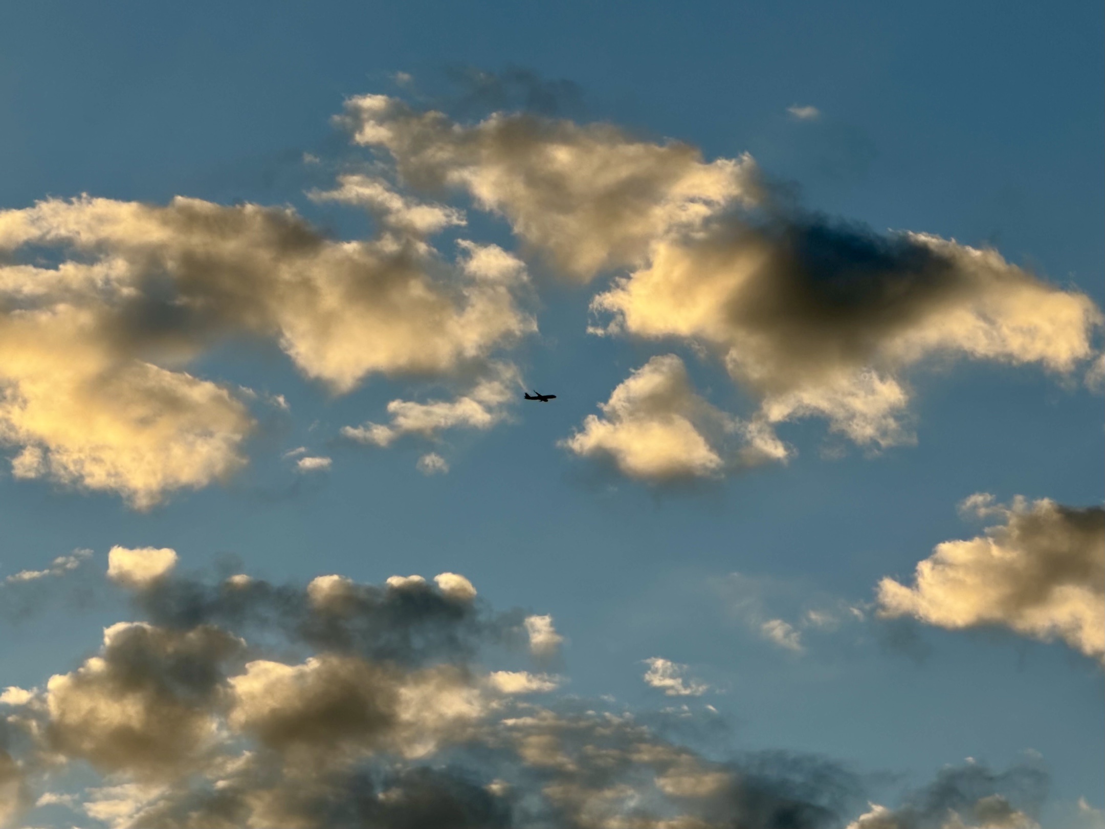 A small plane passing between clouds lit by the evening sun.